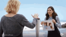 two women are standing next to each other on a beach . one of the women is holding a picture of herself .