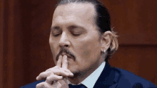 a man with a mustache and a ponytail is holding his finger to his mouth