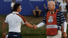 two men are shaking hands on a golf course . one of the men is wearing a red vest with the number 40 on it .