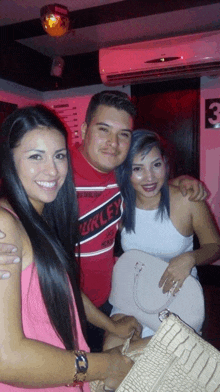 a man wearing a red shirt that says hurley poses for a picture with two women