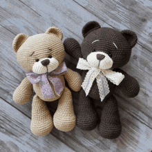 two crocheted teddy bears with bows on their heads are sitting on a wooden table .