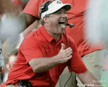 a man in a red shirt and white hat is laughing with his tongue out while wearing a microphone .