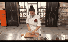 a woman in a chef 's uniform is cutting vegetables on a cutting board in front of a sign that says top chef