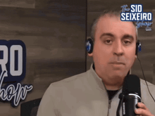a man wearing headphones is talking into a microphone in front of a sign that says the sid seixeiro show