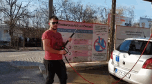 a man is washing a car with a hose in front of a sign that says " onkiszolgalo automoso "