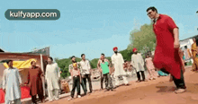 a man in a red shirt is dancing in front of a group of people on a dirt road .