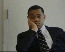 a man in a suit and tie is holding his hand to his face .