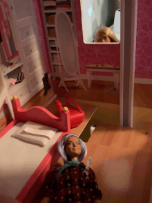 a barbie doll laying on a bed in a dollhouse