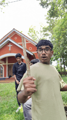 a man with glasses holds a stick in front of a church with a cross on it