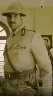 a man in a military uniform and hat is standing in a room in a black and white photo .