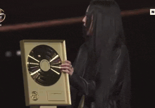 a woman in a black jacket is holding a gold plaque in her hands .