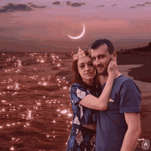 a man and a woman are posing for a picture on a beach with a crescent moon in the background