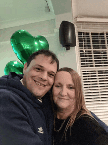 a man and a woman are posing for a picture with green balloons in the background