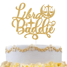 a white cake with gold flowers and a gold cake topper that says libra battle