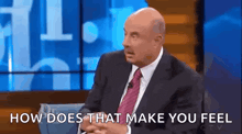 a bald man in a suit and tie is sitting on a stage and talking to someone .