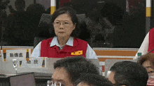 a woman in a red vest sits at a table with a name tag that says ' a ' on it