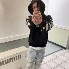 a young man in a black hoodie and jeans is pointing a gun at the camera .