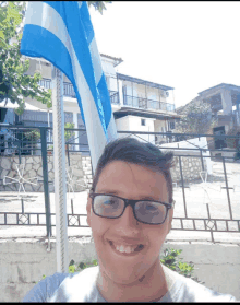 a young man wearing glasses stands in front of a blue and white flag