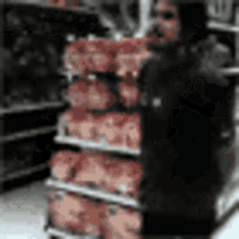 a man in a black jacket is standing in front of a stack of chickens in a grocery store .