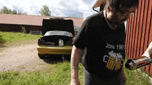 a man in a black shirt is standing in front of a yellow car with the hood up .