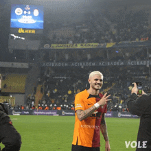 a man taking a picture of a soccer player on a field that says vole on it