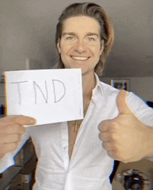 a man in a white shirt holds up a sign that says tnd and gives a thumbs up