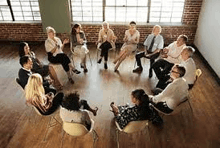 a group of people are sitting in chairs in a circle in a room .