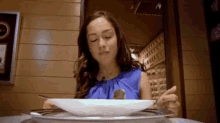 a woman in a blue shirt is sitting at a table with a plate of food in front of her