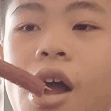 a close up of a young boy eating a sausage with a toothpick in his mouth .