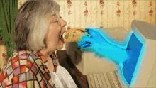 an elderly woman eating a sandwich with a hand coming out of the computer screen