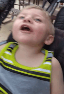 a young boy in a green and gray striped tank top looks up at the sky