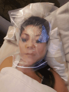 a woman laying in bed with a plastic bag on her face