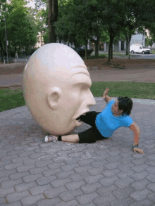 a woman is laying on the ground next to a large statue of a head