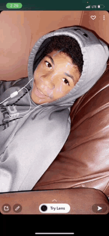 a young boy wearing a grey hoodie is sitting on a couch with a snapchat app open on his phone