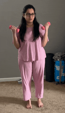 a woman in pink pajamas is holding two pink dumbbells in her hands