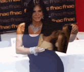 a woman in a blue dress holds a picture of a woman 's neck in front of a fnac sign