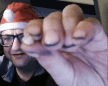 a man wearing a santa hat and glasses is holding his hand up in front of his face .