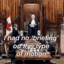 a man in a suit is giving a speech in front of a group of people sitting around a table ..