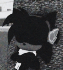 a black stuffed animal with a white bow tie is sitting on a rock