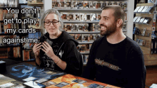 a man and a woman sitting at a table with a sign that says you don t get to play my cards