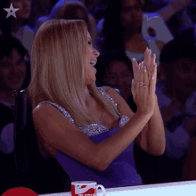 a woman in a purple dress is clapping her hands in front of a cup that says coca cola on it