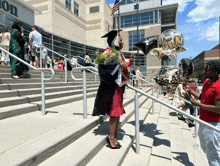 a woman in a graduation cap and gown stands on a set of stairs holding balloons that say congratulations grad