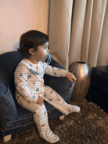 a baby with a pacifier in his mouth sitting on a chair