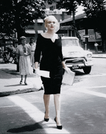 a woman in a black dress is crossing a street in front of a sign that says krena st