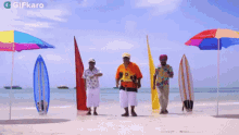 a group of men are dancing on a beach with surfboards and umbrellas and a gifkaro logo in the corner