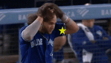 a blue jays baseball player is scratching his head while wearing a blue jersey with a yellow star on it .