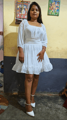 a woman in a white dress and white heels stands in front of a wall with a calendar on it