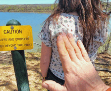 a woman stands in front of a sign that says caution cliffs and dropoffs just beyond this point