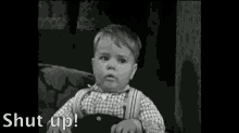 a black and white photo of a little boy sitting in a chair with his eyes closed and the words `` shut up '' behind him .