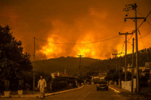 a man walks down a street in front of a burning hillside